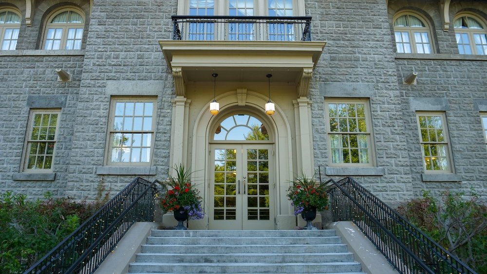 St. Eugene Golf Resort & Casino in Cranbrook, British Columbia, showing the main entrance of the historic Mission Building with stone façade, arched doorway, steps, and hanging lights, highlighting the formal arrival point of the former mission site.