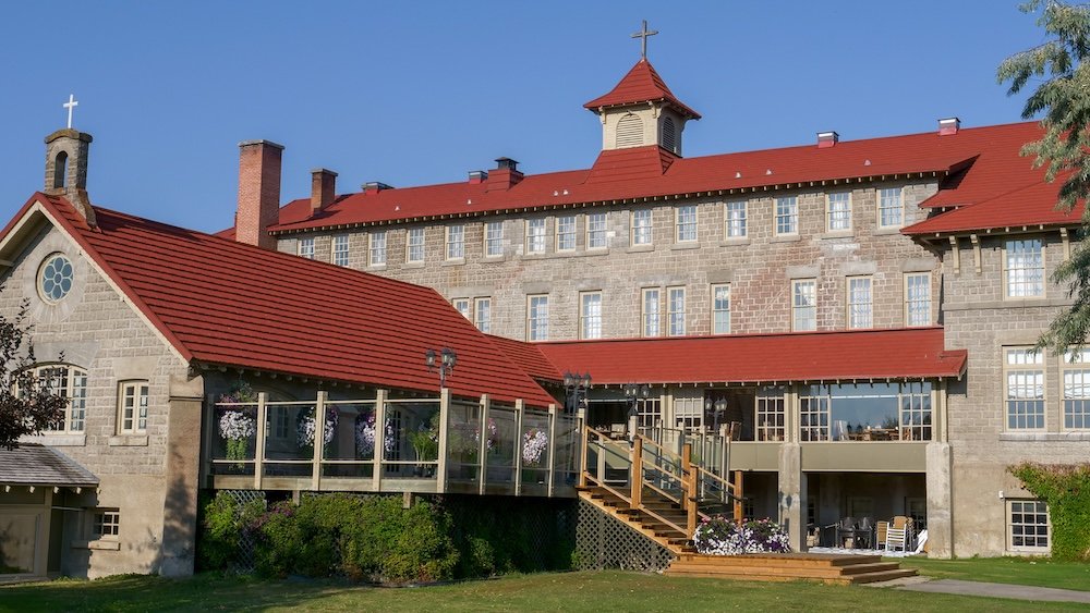St. Eugene Golf Resort & Casino in Cranbrook, British Columbia, showing the rear view of the historic Mission Building with its stone façade, red rooflines, and garden-facing terrace, highlighting the scale and setting of the former mission site.