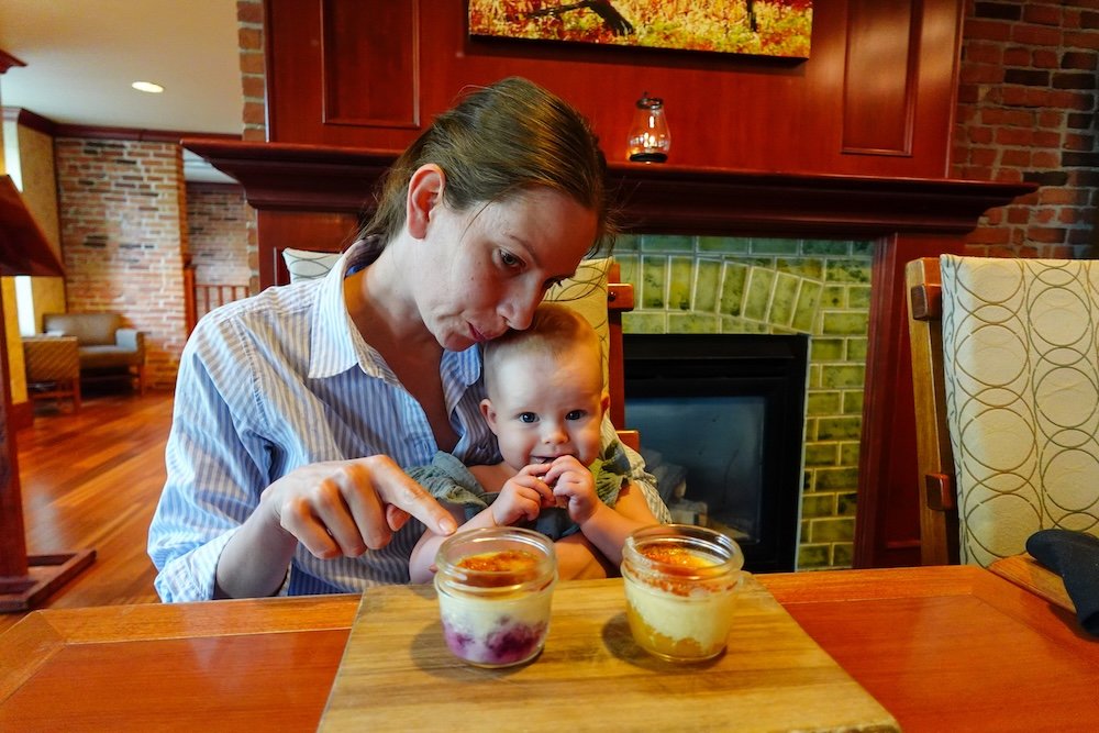 St. Eugene Golf Resort & Casino in Cranbrook, British Columbia, showing Audrey Bergner sharing an excited dessert moment with baby Aurelia at Numa Lounge & Dining, as crème brûlée is served inside the historic Mission Building.