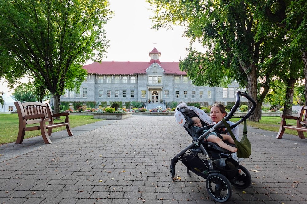 Family-friendly stroller visit to St. Eugene Mission near Cranbrook, BC St. Eugene Mission near Cranbrook, BC during a family stroller visit, with Audrey Bergner pushing baby Aurelia along the paved grounds, highlighting how this historic site and resort is calm, accessible, and well suited for parents traveling with babies or toddlers.