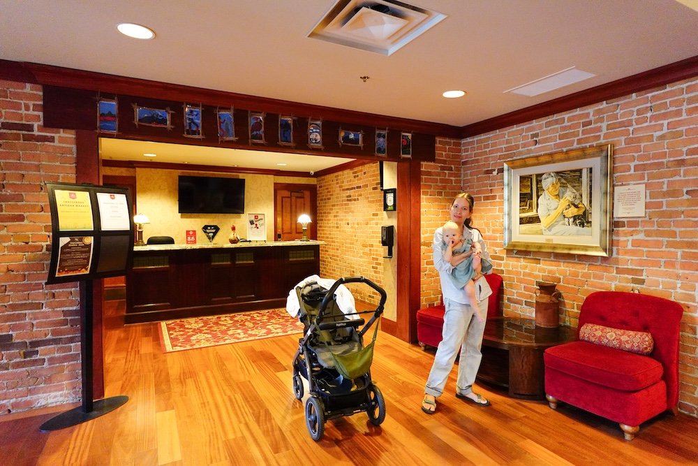 St. Eugene Mission in Cranbrook, BC, showing the historic interior lobby as Audrey Bergner stands with baby Aurelia during a calm family visit, highlighting how this meaningful heritage site can be explored comfortably and thoughtfully with young children.