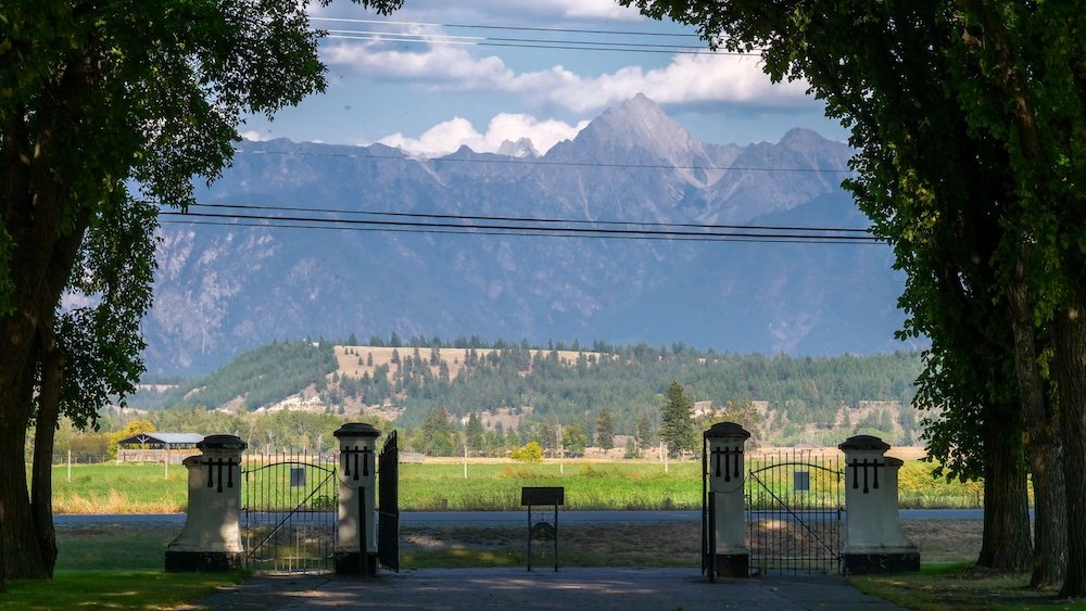 St. Eugene Mission Resort near Cranbrook, British Columbia in summer, with framed mountain views through historic gates, open green fields, and distant peaks, showing one of the most scenic and peaceful heritage settings in the Kootenays.