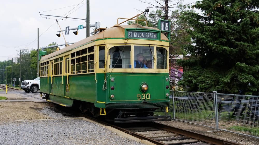 Green-and-cream High Level Bridge Streetcar number 930 approaches along the tracks in Edmonton, Alberta, Canada, displaying its historic St Kilda Beach destination sign beneath the overhead wires.