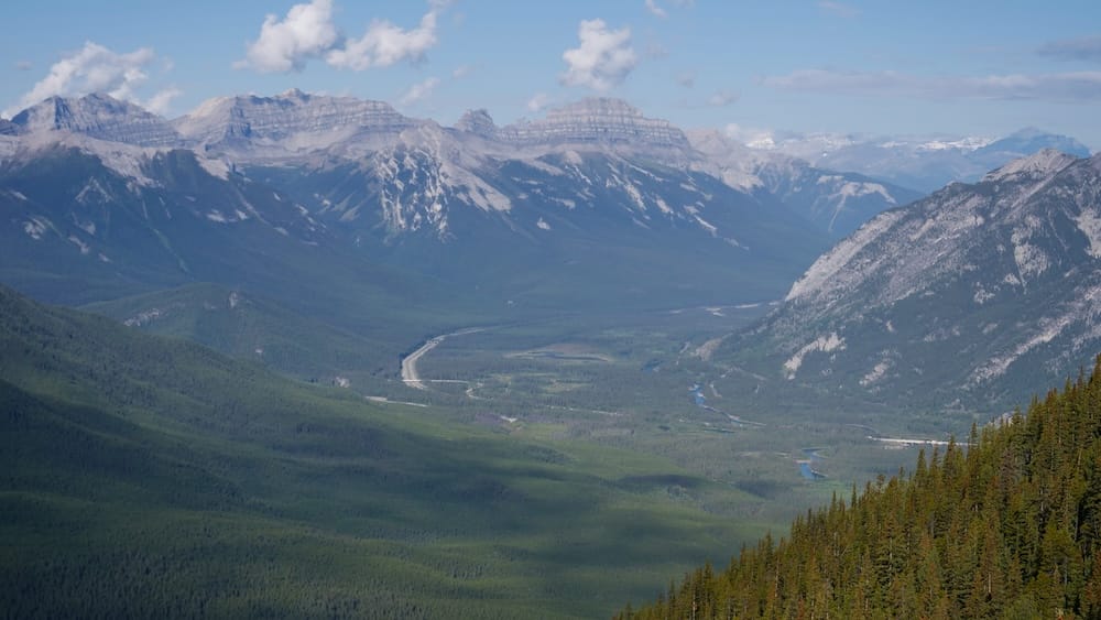 Panorama de Bow Valley y las Montañas Rocosas desde la pasarela de Sulphur Mountain sobre Banff, Alberta, Canadá Amplio panorama montañoso desde la pasarela de Sulphur Mountain sobre Banff, Alberta, Canadá, mirando sobre un valle boscoso hacia capas de las Montañas Rocosas canadienses, con una ruta y un río sinuoso visibles muy abajo.