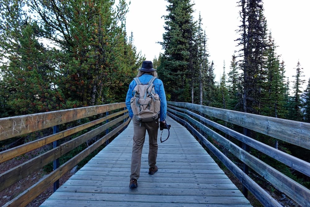Samuel Jeffery en la pasarela de Sulphur Mountain sobre Banff, Alberta, Canadá, cerca de la cumbre de la Banff Gondola Samuel Jeffery caminando por la pasarela de madera de Sulphur Mountain cerca de la parte superior de la Banff Gondola sobre Banff, Alberta, Canadá, con bosque a ambos lados y una cámara en la mano sobre la ruta de la cresta.
