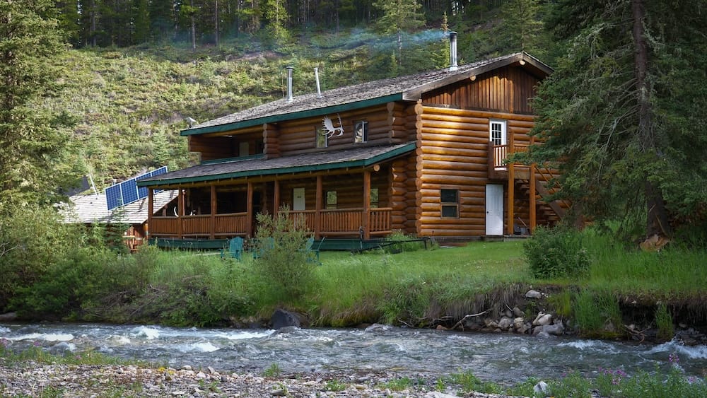 Sundance Lodge in Banff National Park, Alberta, Canada, a rustic log backcountry lodge beside a flowing creek and surrounded by dense evergreen forest.