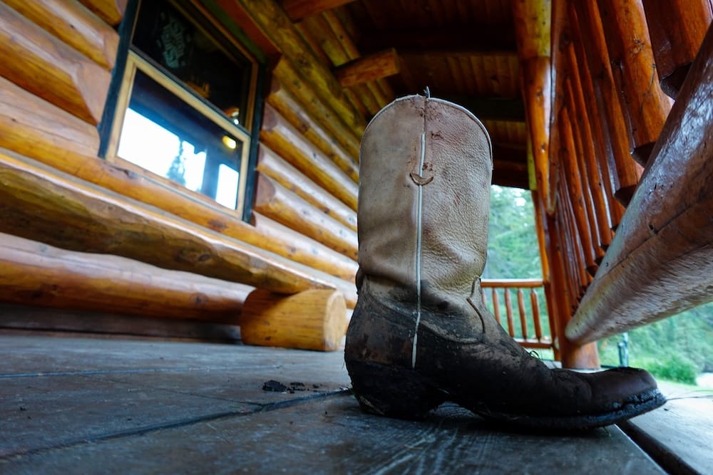Bota vaquera en la galería de Sundance Lodge, Parque Nacional Banff, Alberta, Canadá, durante una travesía a caballo Una bota vaquera gastada sobre la galería de madera de Sundance Lodge, en el Parque Nacional Banff, Alberta, Canadá, con paredes de troncos, barandas y el entorno rústico de la cabaña alrededor.
