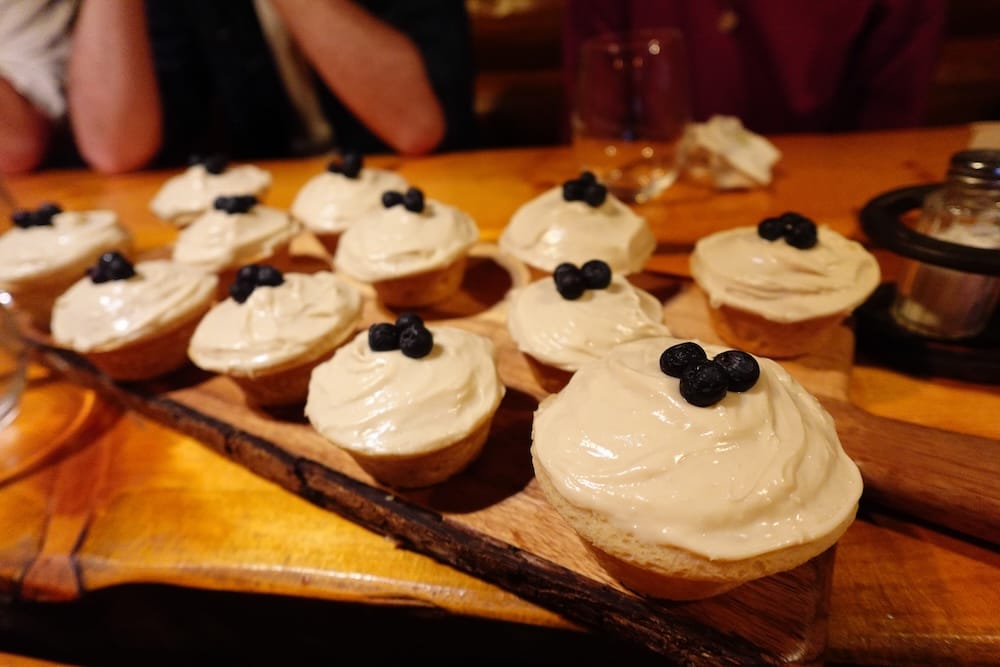 Cupcakes con queso crema en Sundance Lodge durante una travesía a caballo por el Parque Nacional Banff, Alberta, Canadá Cupcakes cubiertos con una capa espesa de frosting de queso crema y arándanos están sobre una tabla de madera en Sundance Lodge, Parque Nacional Banff, Alberta, Canadá, durante una travesía a caballo.