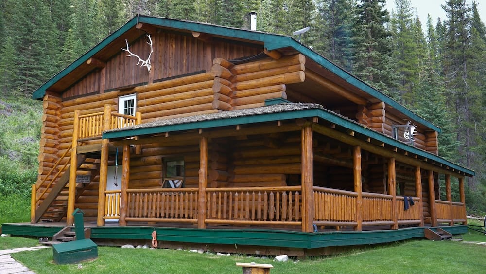 Sundance Lodge en el Parque Nacional Banff, Alberta, Canadá, con arquitectura de troncos y entorno boscoso de backcountry Sundance Lodge en el Parque Nacional Banff, Alberta, Canadá, como una gran cabaña de troncos con galería envolvente, escaleras exteriores y un denso bosque de coníferas alrededor.