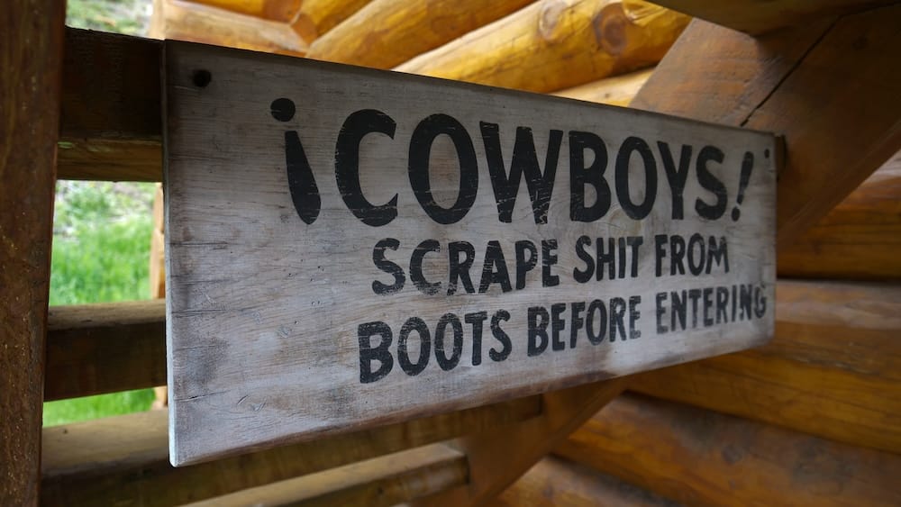 Cartel para limpiar las botas de vaquero en Sundance Lodge, Parque Nacional Banff, Alberta, Canadá, junto a la entrada del lodge de troncos Cartel rústico de madera en Sundance Lodge, Parque Nacional Banff, Alberta, Canadá, que recuerda a los vaqueros limpiar la suciedad de las botas antes de entrar al lodge de troncos.