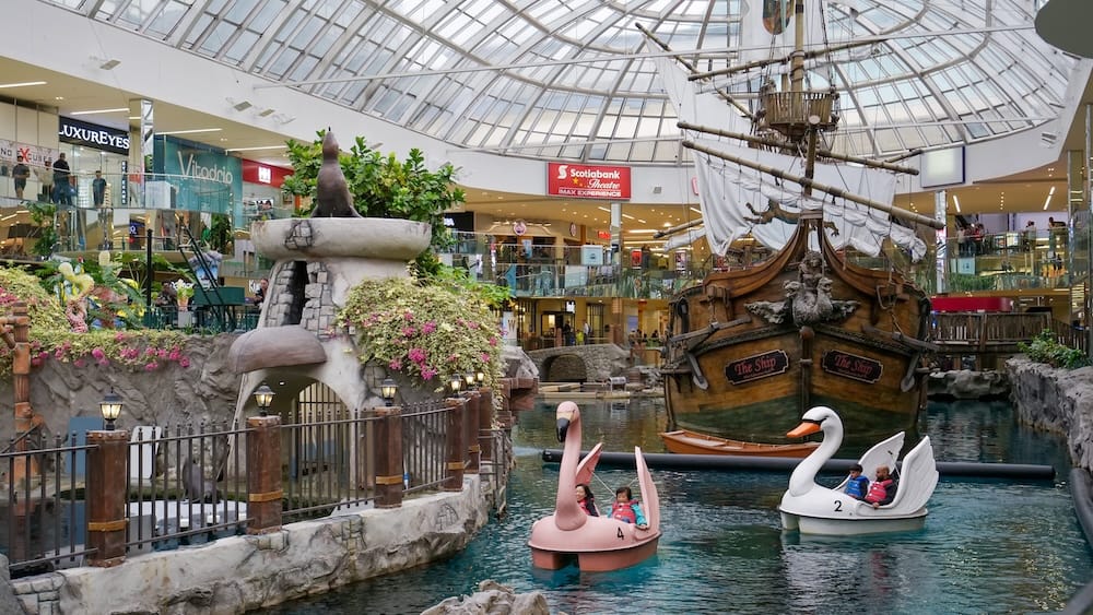 Swan Paddle Boats and Pirate Ship at West Edmonton Mall in Edmonton Visitors riding pink and white swan-shaped paddle boats beside the replica pirate ship and indoor lagoon at West Edmonton Mall in Edmonton, Alberta, beneath the glass atrium roof.