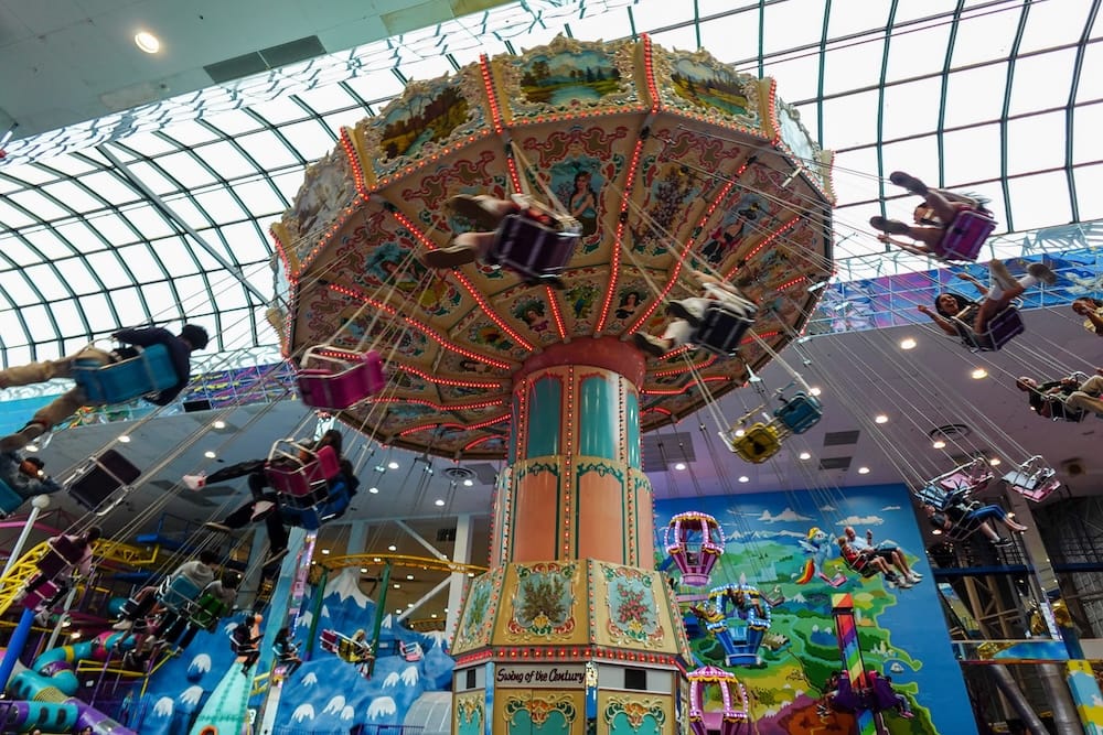 Swing of the Century Ride, Galaxyland, West Edmonton Mall, Alberta, Canada Riders swing through the air on the Swing of the Century ride at Galaxyland inside West Edmonton Mall, Alberta, Canada, beneath the mall's curved glass roof and a painted mural backdrop.