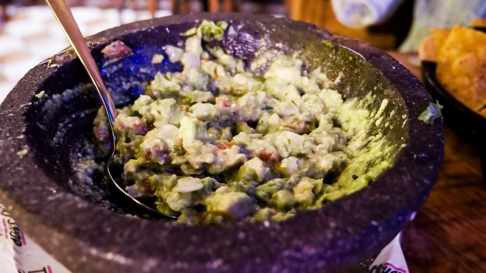 Guacamole Preparado en la Mesa en un Molcajete en Taco Shop, Bourbon Street, West Edmonton Mall, Alberta, Canadá Guacamole recién machacado con tomate y cebolla picados en un molcajete de piedra con una cuchara, servido junto con nachos de maíz en Taco Shop, Bourbon Street, West Edmonton Mall, Alberta, Canadá.