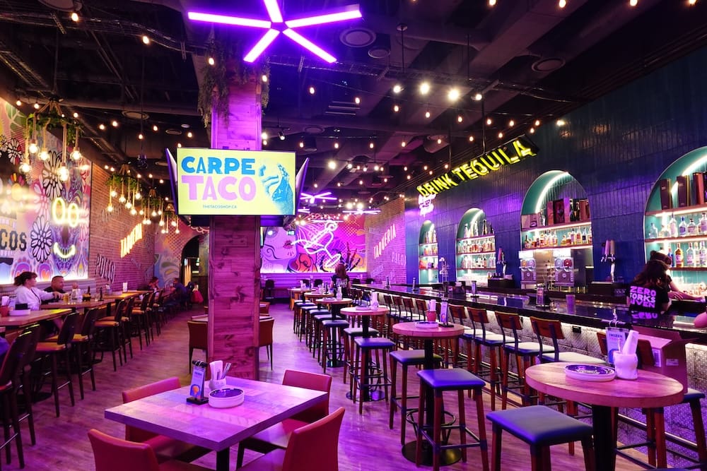 Interior of The Taco Shop in West Edmonton Mall, Edmonton, Alberta, Canada Interior of The Taco Shop in West Edmonton Mall, Edmonton, Alberta, Canada, with neon lighting, a long tequila bar, high-top seating, colourful murals and a Carpe Taco sign.