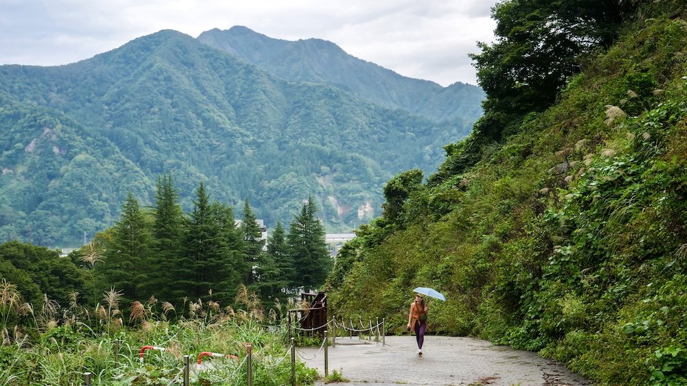 That Backpacker walking in the rain with mountain backdrop in Yuzawa, Japan