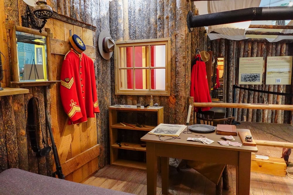 Interior histórico de Fort Calgary en The Confluence con uniformes de la NWMP en Calgary, Alberta, Canadá Interior histórico recreado en The Confluence, Calgary, Alberta, Canadá, con uniformes rojos estilo NWMP, paredes de troncos, escritorio de madera, objetos de época y paneles interpretativos.