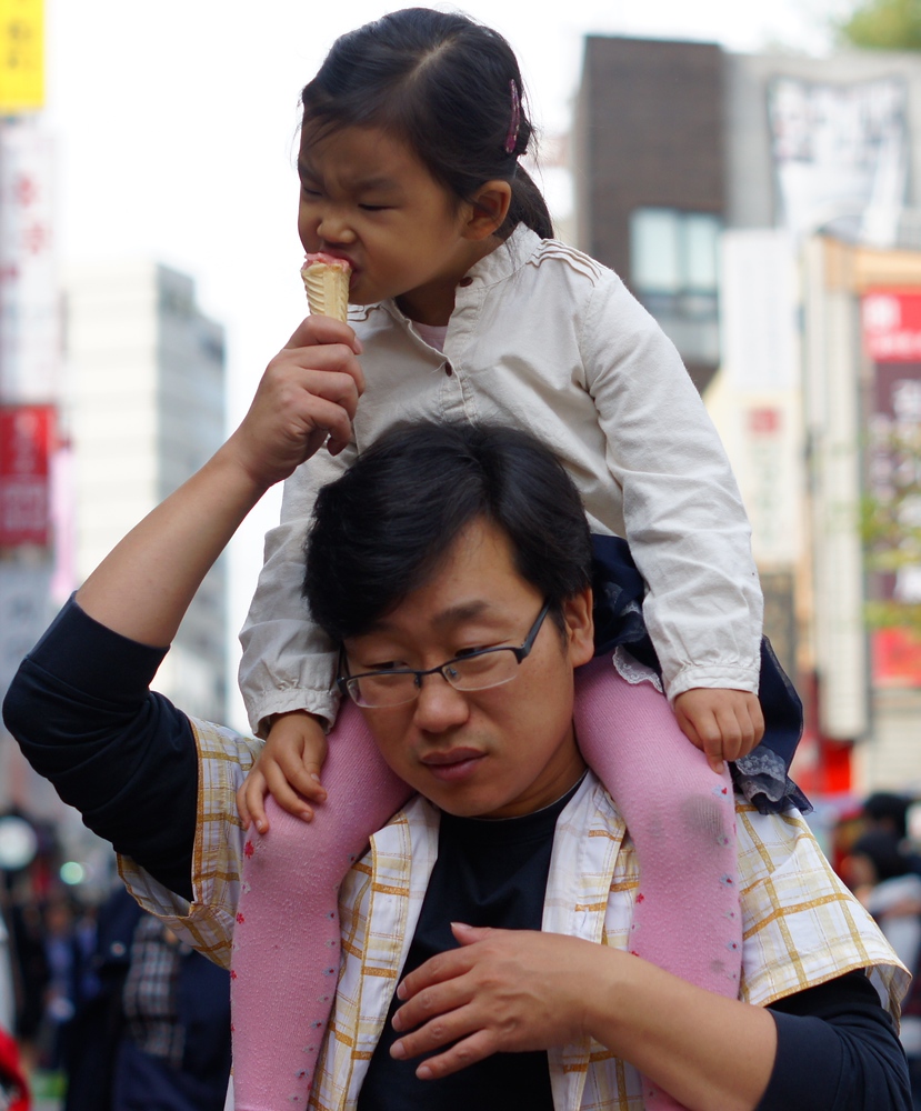 This adorable Korean girls takes a bite out of her ice cream as she's being carried piggyback by her father in what is a very cute moment.