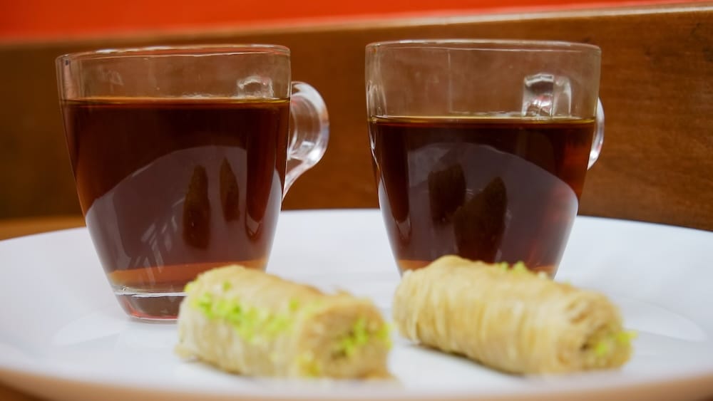 Té turco de cortesía y baklava de pistacho, Top Donair, Jasper Avenue, Centro de Edmonton, Alberta, Canadá Dos tazas de vidrio con té turco al lado de rollos de baklava cubiertos con pistachos en un plato blanco, cortesías servidas en Top Donair en Jasper Avenue, en el centro de Edmonton, Alberta, Canadá.