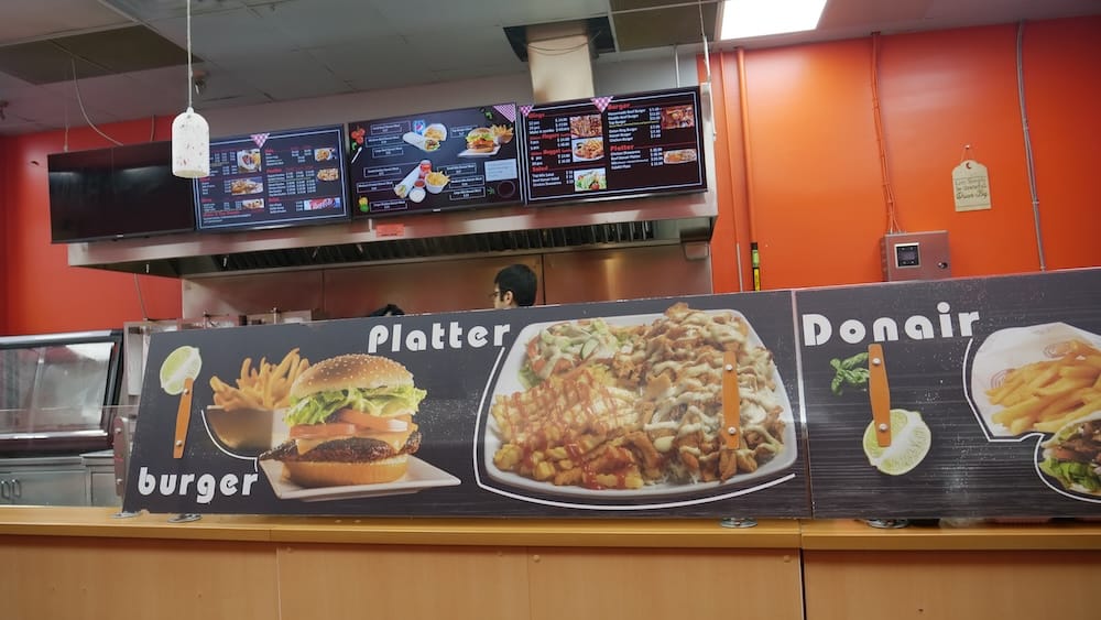 Mostrador de pedidos y cartel del menú, Top Donair, Jasper Avenue, Centro de Edmonton, Alberta, Canadá Mostrador interior de Top Donair en Jasper Avenue, en el centro de Edmonton, Alberta, Canadá, que muestra pantallas digitales con el menú y un cartel en la pared anunciando opciones de hamburguesas, platos y donairs por encima del área para pedir.