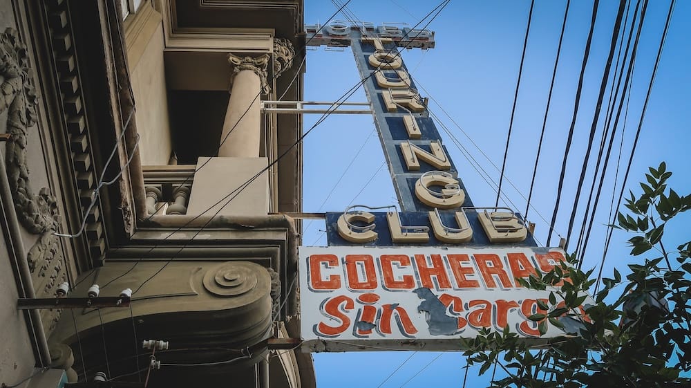 Vintage Touring Club Hotel Sign Beside Historic Architecture in Trelew, Chubut, Argentina A weathered vertical Touring Club Hotel sign rises beside an ornate historic building beneath a clear blue sky in central Trelew, Chubut, Patagonia, Argentina.
