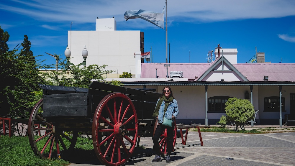 Trelew Patagonia town square in Chubut Argentina with Audrey Bergner standing beside a historic wagon outside a railway building, reflecting the heritage of the Welsh settlement and the transport hub of the Lower Chubut Valley in Patagonia.