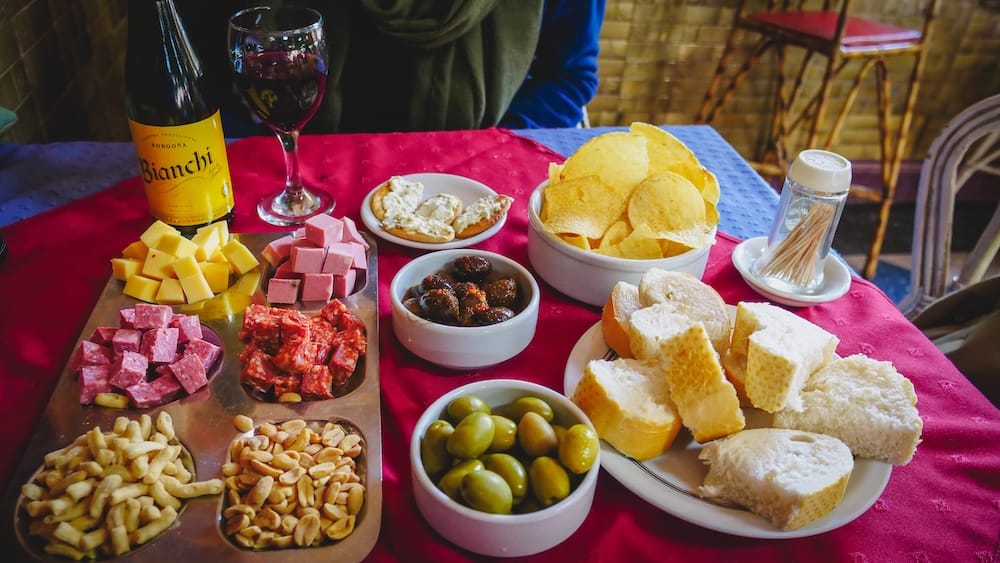 Traditional picada with cured meats, cheeses, olives, bread, and snacks at Touring Club in Trelew, Patagonia, Argentina, showcasing the classic food pairing culture that makes craft beer in the region a hearty, social, and calorie-rich experience.
