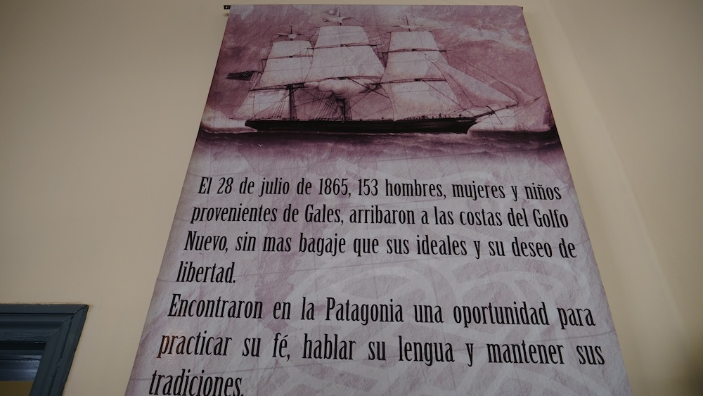 Trelew Patagonia museum poster describing the 1865 arrival of Welsh settlers to Golfo Nuevo in Chubut Argentina featuring a sailing ship illustration and historical Spanish text explaining the migration of Welsh families to Patagonia.