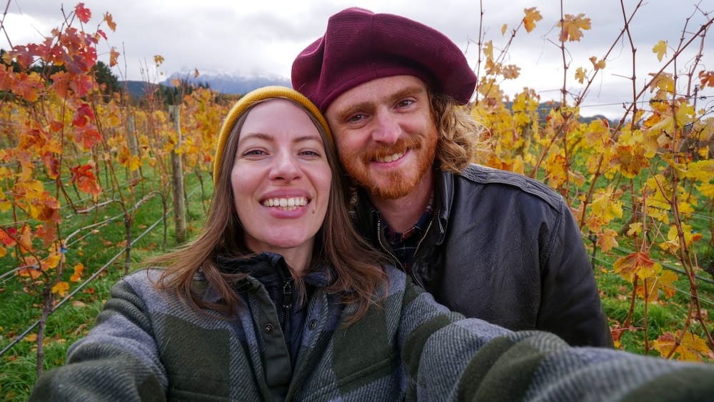 Audrey Bergner and Samuel Jeffery in an autumn vineyard at Trevelin, Chubut, Patagonia, Argentina Audrey Bergner and Samuel Jeffery smile for a selfie among rows of autumn grapevines in Trevelin, Chubut, Patagonia, Argentina, wearing warm jackets beneath an overcast mountain sky.