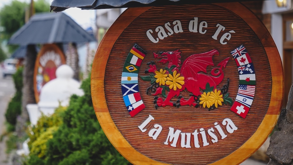 Trevelin Patagonia Casa de Té La Mutisia Welsh tea house sign in Chubut Argentina featuring a red Welsh dragon and international flags representing the multicultural heritage of the historic Welsh settlement town in Patagonia.