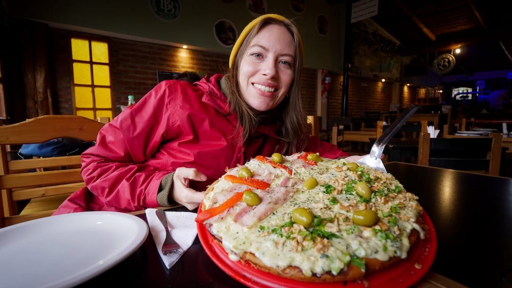 Trevelin Patagonia Argentina Audrey Bergner enjoying walnut topped Patagonian pizza with olives herbs and melted cheese inside cozy restaurant highlighting Welsh influenced regional cuisine and authentic travel food experience