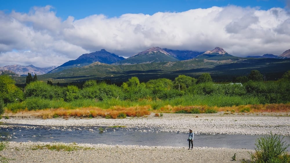 Trevelin Patagonia Audrey Bergner standing by a river with expansive mountain views and lush greenery in the Andes foothills highlighting the wide open landscapes and natural beauty that make this region feel immersive and worth staying longer