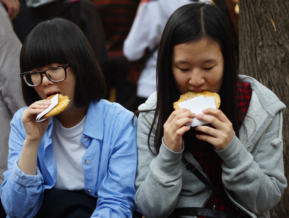 Two Korean girls enjoy hotteok 호떡(Korean style pancake filled with brown sugar, peanuts, cinnamon & honey) in Insadong, Korea.