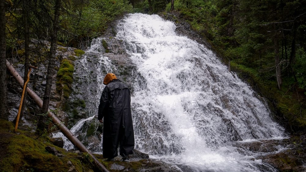 Cascada sin nombre, caminata al lago Matthias, Halfway Lodge, Parque Nacional Banff, Alberta, Canadá Un senderista con ropa de lluvia hace una pausa junto a una cascada sin nombre en la caminata al lago Matthias cerca de Halfway Lodge en el Parque Nacional Banff, Alberta, Canadá.