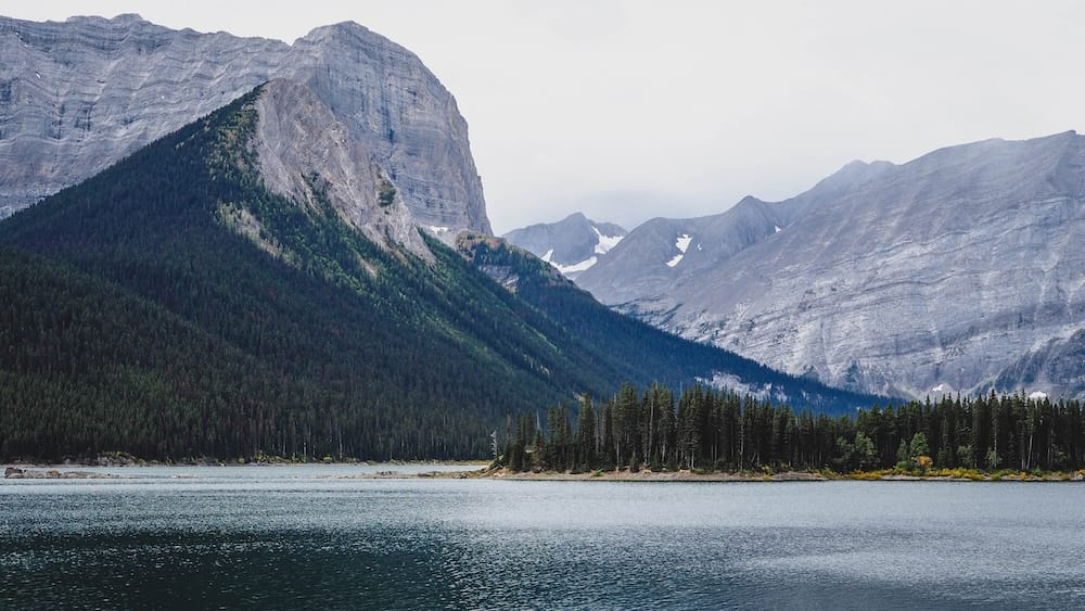 Panoramic mountain view at Upper Kananaskis Lake, Peter Lougheed Provincial Park, Alberta A panoramic view across Upper Kananaskis Lake toward a sharp triangular peak and a snow-streaked mountain range in Peter Lougheed Provincial Park, Alberta.