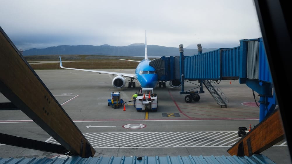 Commercial Jet at Ushuaia Airport in Tierra del Fuego, Patagonia, Argentina A blue commercial jet stands at the gate with ground crews and a boarding bridge at Ushuaia Airport in Tierra del Fuego, Patagonia, Argentina, beneath low cloud over distant hills.