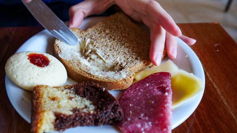 Close-up of breakfast at Vertical Lodge in El Chaltén, Santa Cruz, Patagonia, Argentina, with brown bread, butter, cheese, salami, cake and a jam-filled pastry on a white plate.