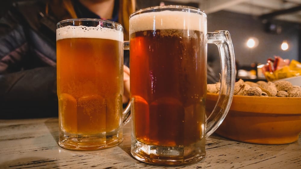 Two large mugs of Patagonian craft beer served with bowls of peanuts inside a cozy bar in Villa La Angostura, Argentina, capturing the relaxed mountain-town drinking culture where simple snacks and cold pints follow long days exploring the Andean Lake District.

