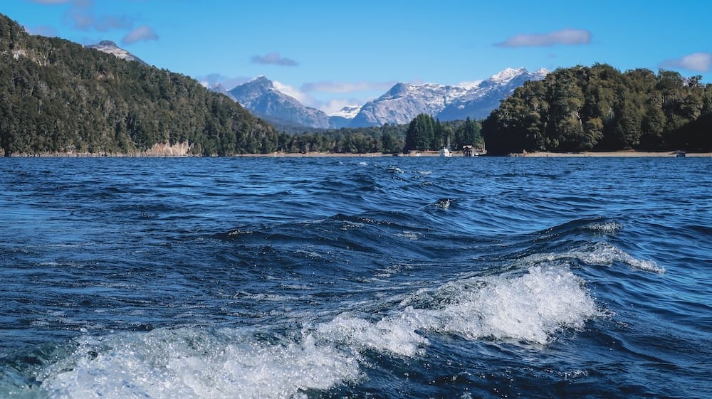 Wind-driven waves across a Patagonian lake near Villa La Angostura with snowcapped Andes peaks in the background, showing how even scenic northern Patagonia waters become choppy and unpredictable under sustained gusts.
