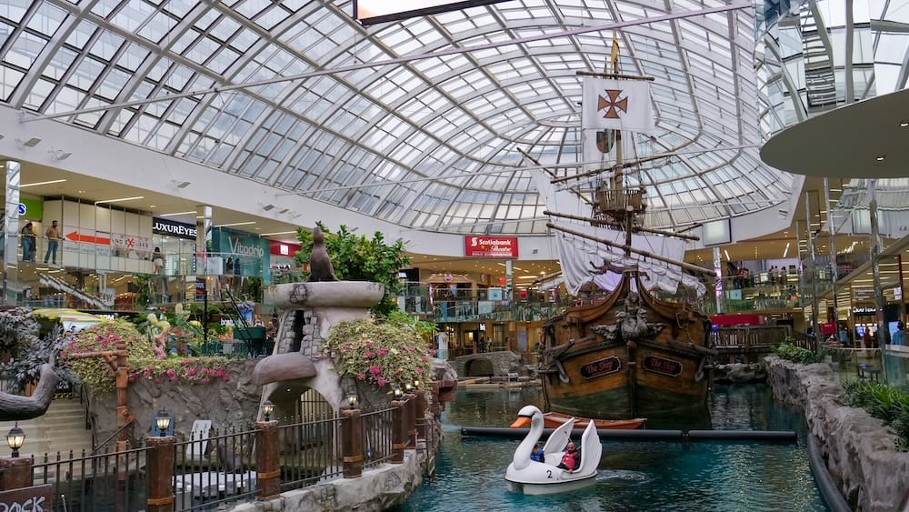 Replica Pirate Ship and Swan Paddle Boat at Deep Sea Adventure Lake, West Edmonton Mall, Edmonton, Alberta, Canada A replica pirate ship floats in the indoor Deep Sea Adventure Lake at West Edmonton Mall in Edmonton, Alberta, Canada, beneath a curved glass atrium roof, with a swan-shaped paddle boat and rockwork sea lion statue nearby.