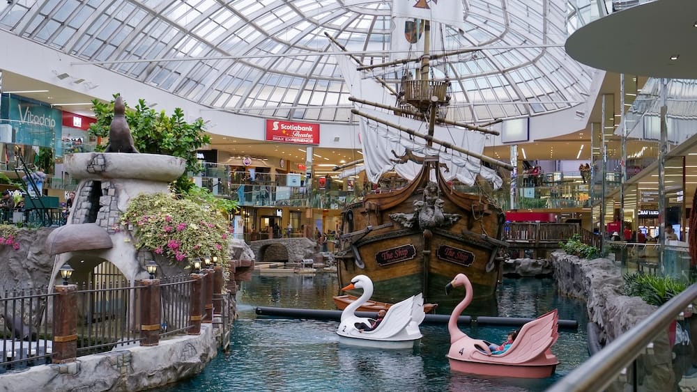 Un gran barco pirata se encuentra dentro de West Edmonton Mall en Edmonton, Alberta, Canadá, bajo un techo de vidrio, rodeado de agua interior, botes con forma de cisne, tiendas, pasarelas y atracciones.