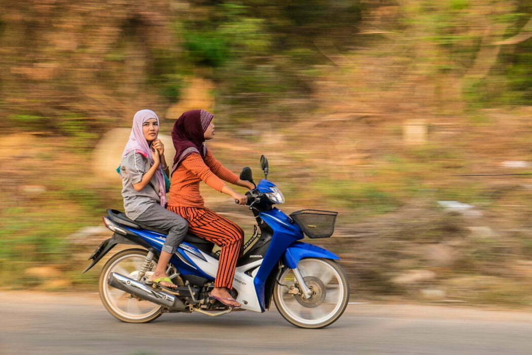 When the eye of a camera meets human eyes. Two young girls riding a scooter in the almost deserted southern tip of Koh Lanta, Thailand. 