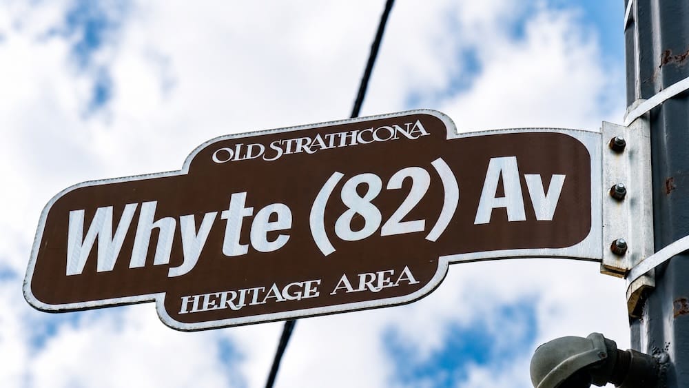 Cartel de Whyte Avenue y el área patrimonial de Old Strathcona, Edmonton, Alberta, Canadá Un cartel marrón del área patrimonial señala Whyte Avenue, también conocida como 82 Avenue, en Old Strathcona, Edmonton, Alberta, Canadá, montado frente a un cielo claro con nubes dispersas.