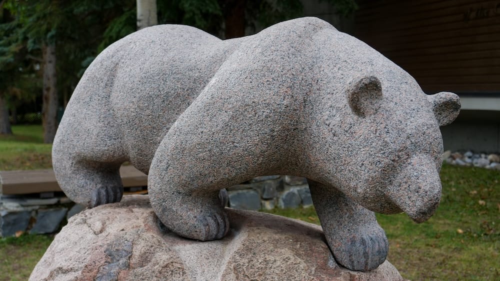 Granite bear cub sculpture, Whyte Museum of the Canadian Rockies grounds, Banff, Alberta A carved granite sculpture of two bear cubs perched on a large boulder, displayed on the outdoor grounds of the Whyte Museum of the Canadian Rockies in Banff, Alberta, Canada.