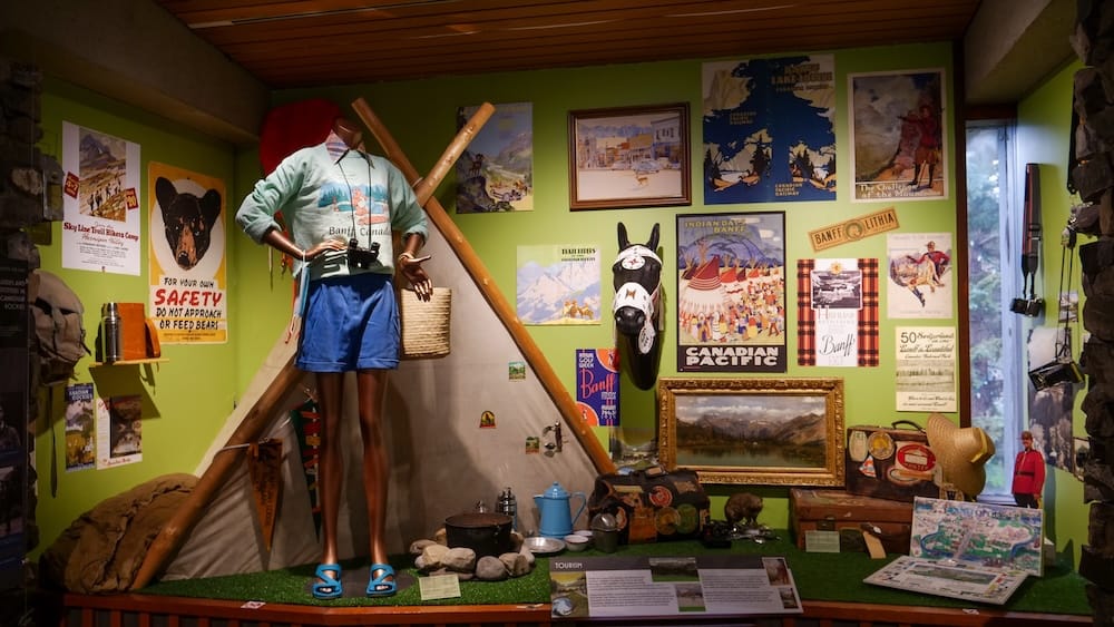 Vintage tourism history exhibit, Heritage Gallery, Whyte Museum of the Canadian Rockies, Banff A tourism-history display at the Whyte Museum of the Canadian Rockies featuring a mannequin in vintage camping gear beside a tent frame, surrounded by old Canadian Pacific travel posters, luggage, and camping equipment, Banff, Alberta, Canada.