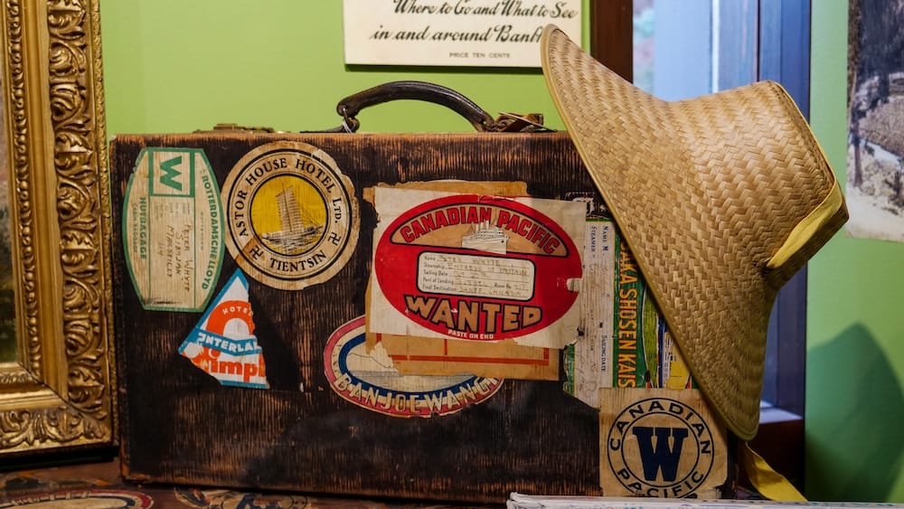 Vintage travel suitcase, archives collection, Whyte Museum of the Canadian Rockies, Banff A weathered vintage suitcase covered in old hotel and steamship travel stickers, including a Canadian Pacific line label, displayed beside a straw hat in the archives collection at the Whyte Museum of the Canadian Rockies, Banff, Alberta.