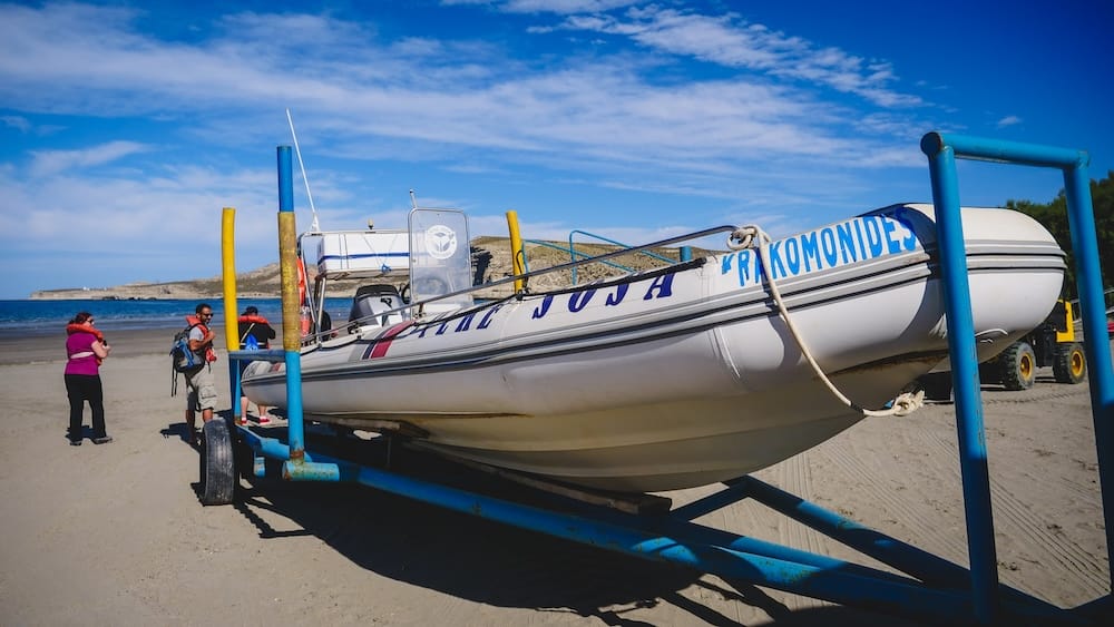 Embarcación para excursiones de fauna sobre la playa de Península Valdés, Chubut, Patagonia, Argentina Una embarcación inflable para excursiones de fauna descansa sobre un tráiler junto a una playa de arena en Península Valdés, Chubut, Patagonia, Argentina, mientras varios pasajeros esperan bajo un cielo azul brillante.
