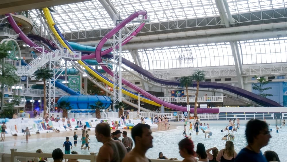 World Waterpark inside West Edmonton Mall in Edmonton, Alberta, Canada, with a large indoor wave pool, colourful twisting waterslides, lounge chairs and crowds of swimmers beneath the glass roof.