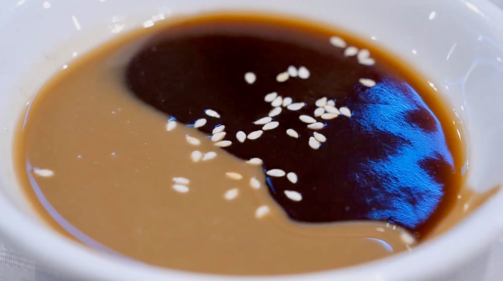 Close-up of a dual dipping sauce with peanut sauce on one side and dark hoisin sauce on the other, sprinkled with sesame seeds, served alongside zhaliang at Chinese Cultural Centre Cuisine in Calgary, Alberta, Canada.
