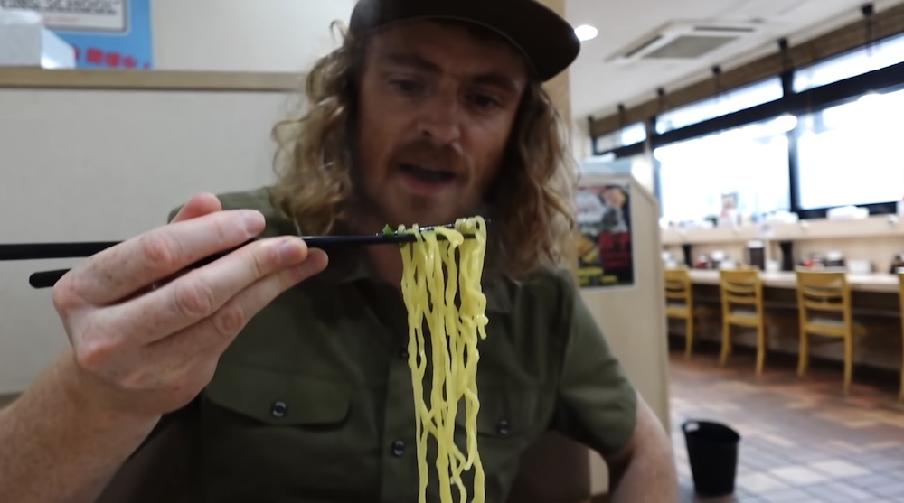 Samuel Jeffery comiendo shio ramen de Hakodate en Yondaime Ramen, Hakodate, Hokkaido, Japón Samuel Jeffery levanta fideos amarillos con palitos mientras come shio ramen en Yondaime Ramen, Hakodate, Hokkaido, Japón, sentado dentro del comedor informal del restaurante.