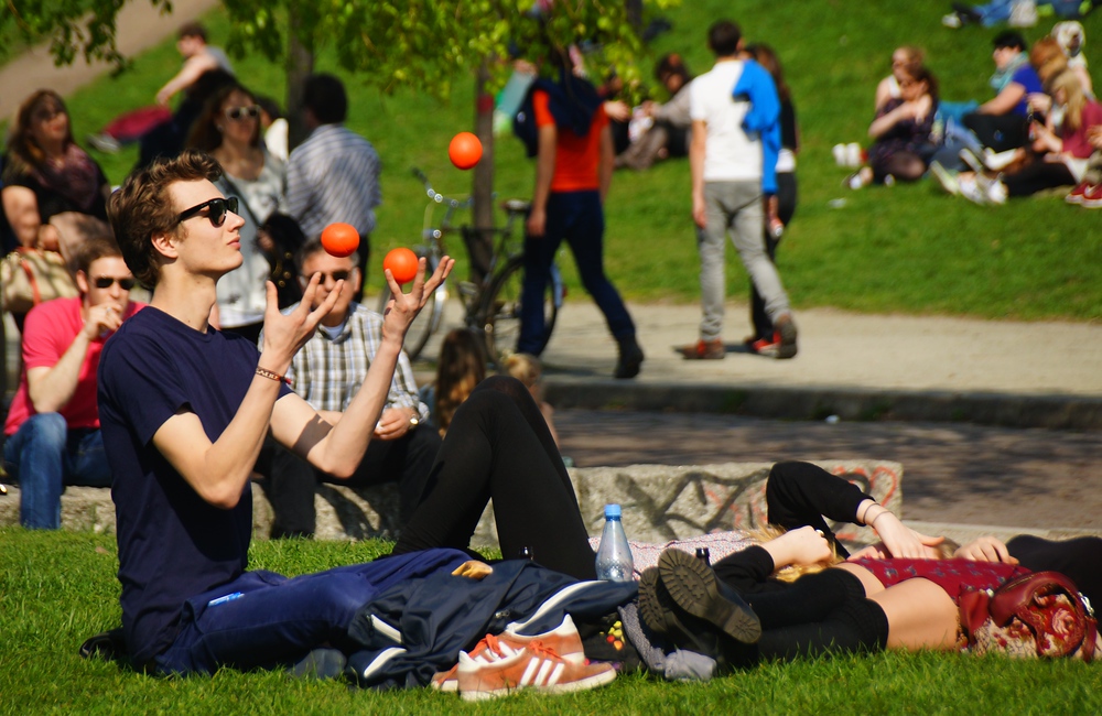 Young man wearing sunglasses and juggling balls while sitting down in Mauerpark, in Berlin, Germany